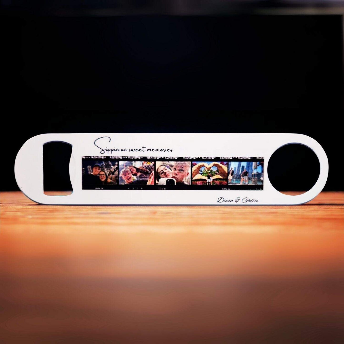A personalized metal bottle opener featuring a custom photo film strip, displayed on a wooden surface with a dark brown, textured background.