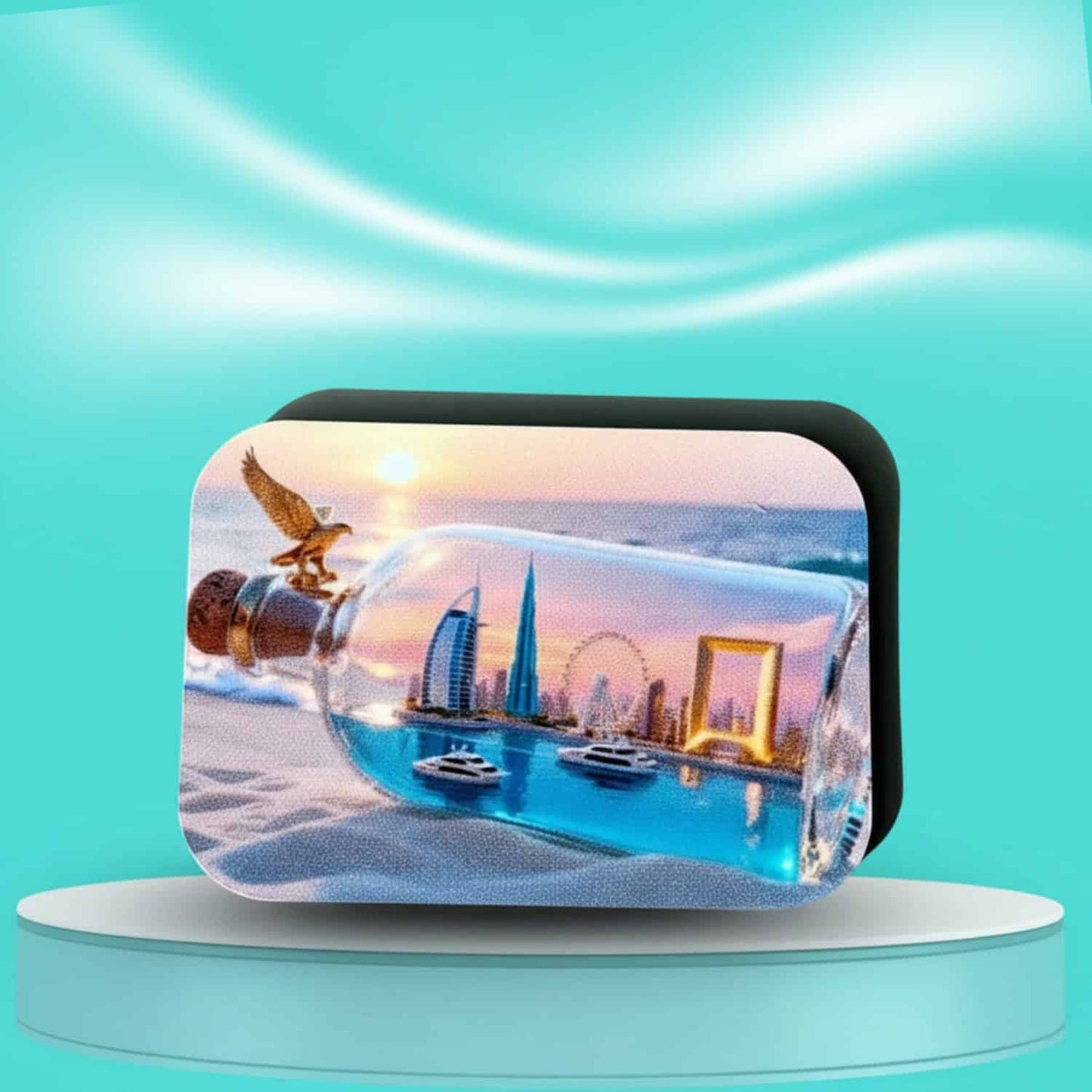 Pre-designed rounded rectangle magnet on a teal and white pedestal, showcasing a miniature Dubai cityscape inside a clear glass bottle lying on a sandy beach, with a golden eagle perched on the cork and a sunset background, all against a bright teal backdrop.