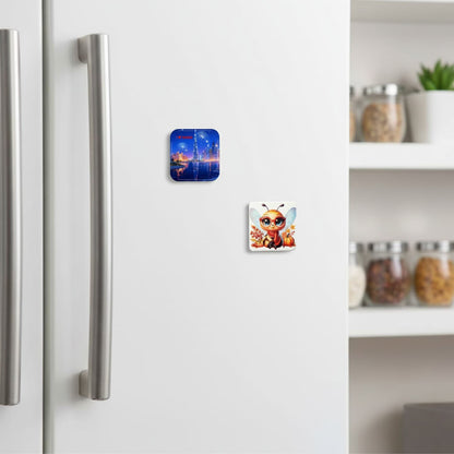 Two 6.5cm rounded square refrigerator magnets displayed on a modern, white fridge door in a kitchen setting. The magnet on the top left features a nighttime illustration of the Dubai skyline with fireworks and the text 'I ❤️ Dubai'. The magnet on the bottom right features a cute, cartoon bee wearing glasses, a red scarf, and sitting amongst autumn elements like pumpkins and leaves.