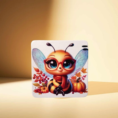 A rounded square magnet, featuring a cute cartoon bee in red glasses, surrounded by autumn leaves and a pumpkin, displayed on a warm, solid light brown background.