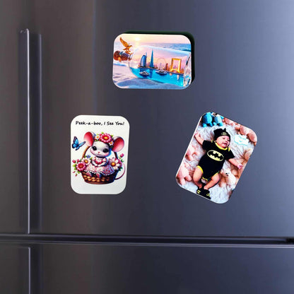 Collection of three custom-printed, rounded rectangle magnets from InkFluenceME on a modern silver fridge. The magnets display a Dubai cityscape, an adorable baby in a Batman onesie, and a cheerful cartoon mouse in a flower basket. This image showcases personalized souvenirs and custom photo magnets.