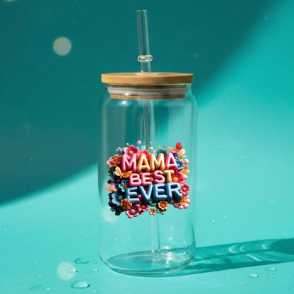 InkFluenceME custom UV Printed 16oz Plastic Tumbler featuring the vibrant, multi-colored text 'MAMA BEST EVER' surrounded by detailed flowers and butterflies, with a bamboo lid and glass straw, set on a bright teal background with water droplets.