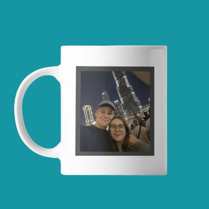 Personalized photo mug featuring a couple smiling while taking a selfie at night in Dubai, with the brightly lit Burj Khalifa skyscraper visible in the background, set against a solid teal background.
